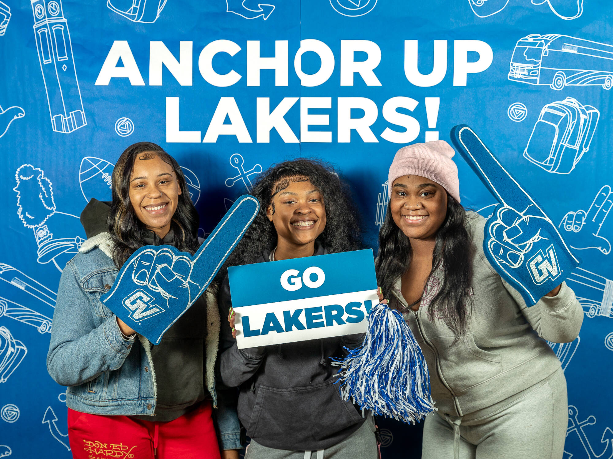 three individuals, one on the left holding up a foam finger, one in the middle holding up a Go Lakers! sign and a pompom, one on the right also holding up a foam finger